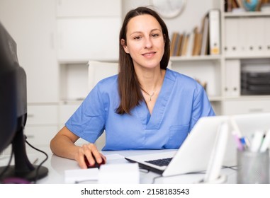 Confident Young Female Doctor Prints An Outpatient Patient Card On A Computer In The Office, Sitting At Her Workplace