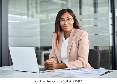 Confident young female lawyer, professional African American business woman company manager executive wearing suit glasses working on laptop in office sitting at desk looking at camera, portrait. - Powered by Shutterstock