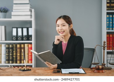 Confident young female lawyer reading a book in her office, surrounded by legal documents and scales, ready to provide legal advice. - Powered by Shutterstock