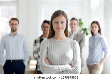 Confident young female leader, office worker, intern or company employee smiling looking at camera with team at background, happy successful businesswoman professional manager business coach portrait - Shutterstock ID 1295995831