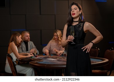 Confident Young Female Poker Player With Glass Of Champagne In Casino