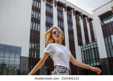 Confident young girl in a white t-shirt and sunglasses walks through the city streets enjoying a summer day. Street photography