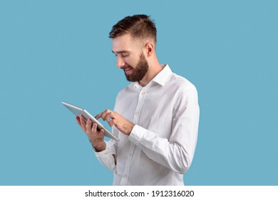 Confident young guy in office wear using tablet computer over blue studio background. Focused freelancer working or studying remotely, having web conference, communicating online - Powered by Shutterstock