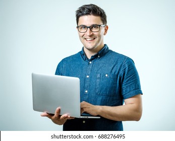 Confident young handsome man in shirt holding laptop while standing against white background