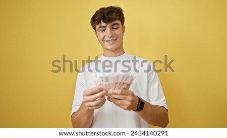 Confident young hispanic teenager counting icelandic krona banknotes, smiling happily against a bright yellow isolated background
