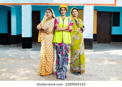 confident young indian female engineer wearing yellow hard hat and vest standing cross arms along with two other women. concept of woman empowerment. Industrial factory workers. Skill india.