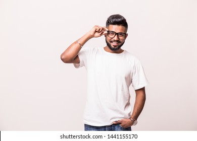 . Confident young Indian man adjusting his eyeglasses and smiling while standing against white background - Powered by Shutterstock