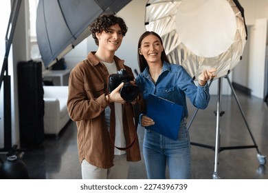 Confident young male photographer talking with his female assistant, preparing for photo or video shooting while woman pointing forwards and smiling - Powered by Shutterstock