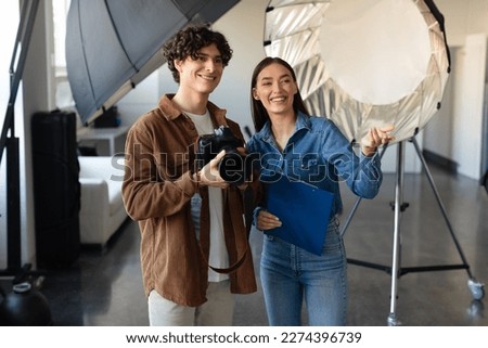 Confident young male photographer talking with his female assistant, preparing for photo or video shooting while woman pointing forwards and smiling