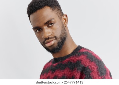 Confident young man with a beard wearing a red and black sweater gazes intently at the camera in a casual setting - Powered by Shutterstock