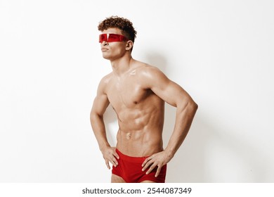 Confident young man with curly hair posing in red sunglasses and swimwear, showcasing fitness and style. Fashion and summer concept for modern lifestyle. - Powered by Shutterstock