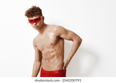 Confident young man with curly hair wearing red sunglasses and red swimwear, displaying a strong physique against a minimalist white background. - Powered by Shutterstock