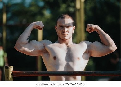 Confident young man flexing his biceps outdoors. Showcasing strength, muscles, and fitness in a sunny outdoor setting. - Powered by Shutterstock