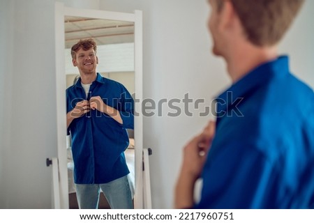 A confident young man getting dressed at the mirror