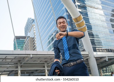 Confident young man holding suit with Briefcase and looking at his watch while standing outdoors with cityscape in the background, In time appointment Concept. - Powered by Shutterstock