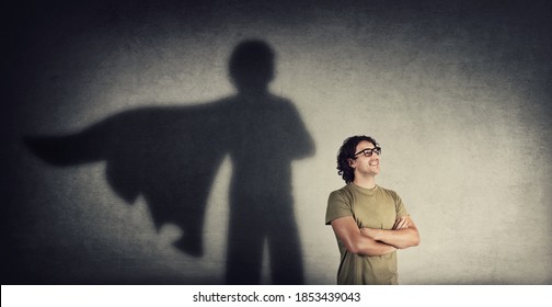 Confident young man keeps arms crossed smiling optimistic as casting a superhero with cape shadow on the wall. Motivated and ambitious guy tends to achieve success. Hero leadership and power concept