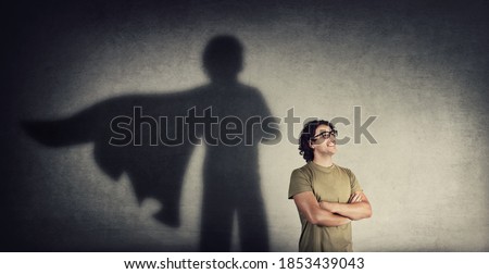 Confident young man keeps arms crossed smiling optimistic as casting a superhero with cape shadow on the wall. Motivated and ambitious guy tends to achieve success. Hero leadership and power concept