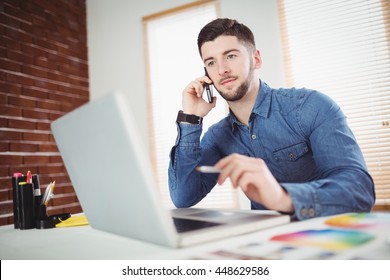 Confident Young Man Talking On Phone In Office