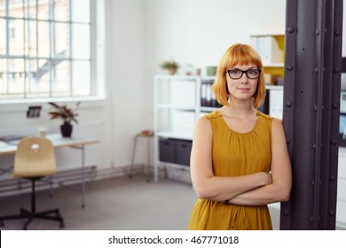 Confident Young Redhead Businesswoman Wearing Glasses Standing Leaning On A Pillar In The Office With Folded Arms And A Quiet Smile, With Copy Space