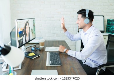 Confident young salesman waving at colleague during video call on computer at desk