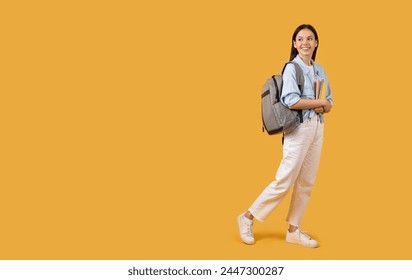 Confident young student walking with a backpack and a stack of books on a bright yellow background, copy space - Powered by Shutterstock