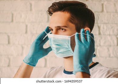 Gewissener junger Chirurgen in Latex-Schutzhandschuhen, die ärztliche Maske im Gesicht tragen. Ein professioneller Arzt in medizinischen Handschuhen auf Schutzmaske. Persönlicher Schutz. Coronavirus COVID-19