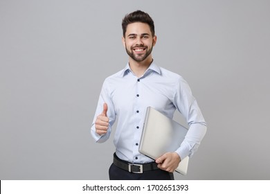 Confident young unshaven business man in light shirt posing isolated on grey wall background. Achievement career wealth business concept. Mock up copy space. Hold laptop pc computer, showing thumb up