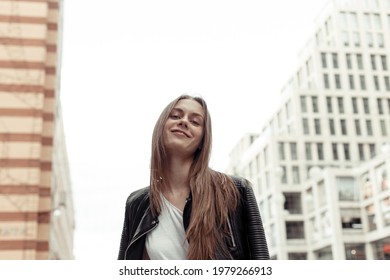 Confident Young Woman From Below Looking Down At Camera. Pretty Girl With Blonde Hair Wearing Black Faux Leather Jacket. Low Angle Shot.