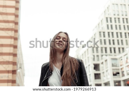 Confident young woman from below looking down at camera. Pretty girl with blonde hair wearing black faux leather jacket. Low angle shot.
