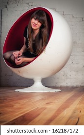 Confident Young Woman In A Black Dress Sitting In Egg Chair.