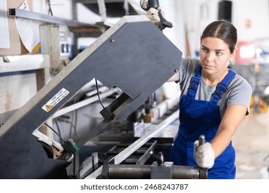 Confident young woman in blue overalls and gloves cutting PVC profile on industrial machine in window production and assembly workshop.. - Powered by Shutterstock