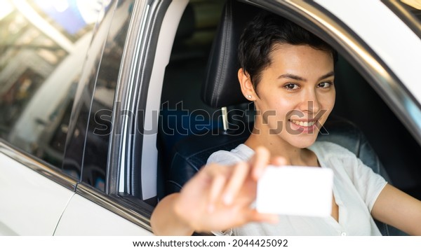 Confident young woman\
driver in car holding blank card mockup. Caucasian woman showing\
new driver\'s license 
