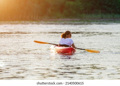 Confident young woman kayaking on river alone with sunset in the backgrounds. Having fun in leisure activity. HÑƒalthy active girl spend weekend outdoors on the kayak boat. Sport, relations concept