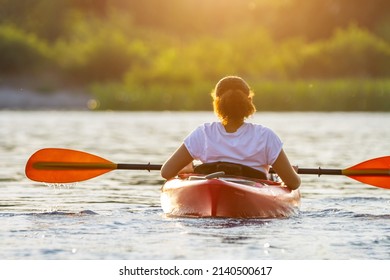 Confident young woman kayaking on river alone with sunset in the backgrounds. Having fun in leisure activity. HÑƒalthy active girl spend weekend outdoors on the kayak boat. Sport, relations concept
