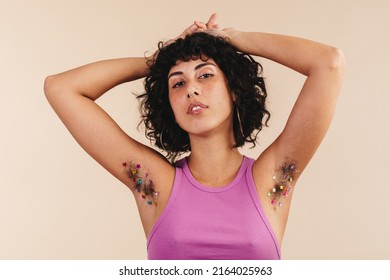 Confident Young Woman Looking At The Camera While Showing Her Confetti-decorated Underarms. Body Positive Young Woman Making The Choice Not To Shave. Young Woman Embracing Her Natural Body Hair.