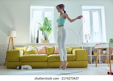 Confident Young Woman In Sports Clothing Jumping With Rope At Home