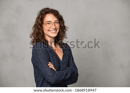 Confident young woman wearing eyeglasses and standing on gray wall. Portrait of smiling businesswoman isolated against grey background with copy space. Proud student girl with specs looking at camera.