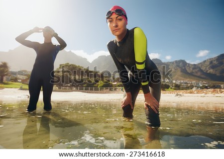 Confident young woman in wet suit standing in water looking at camera. Young triathletes preparing for competition. Triathlon training at the lake.