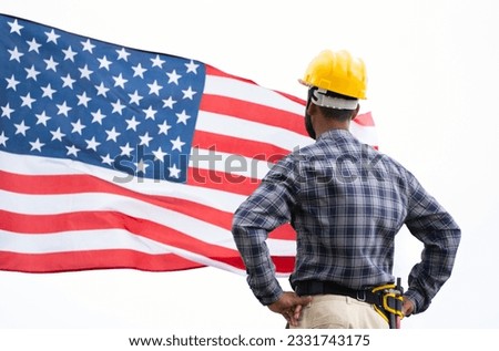 Confidently standing construction working with safety hat in front of waving American Flag - concept of Independence day or Labours day celebration