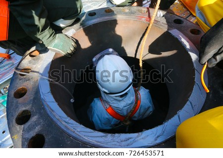 Confined space entry by a worker who wear white chemical suit.