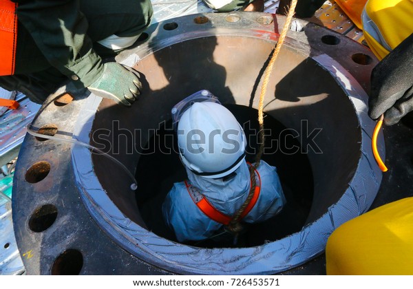Confined space entry by a worker who wear white\
chemical suit.
