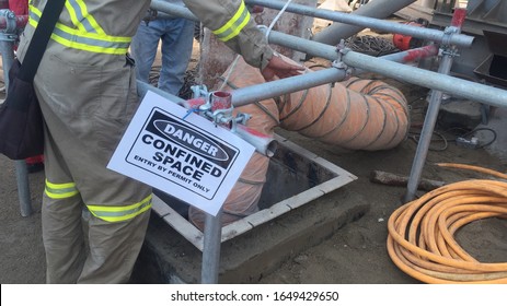 Confined Space Entry Job With Person Observing Entrant Inside The Silo Through The Manhole. Ventilation Through Ducting And Warning Signage At Site