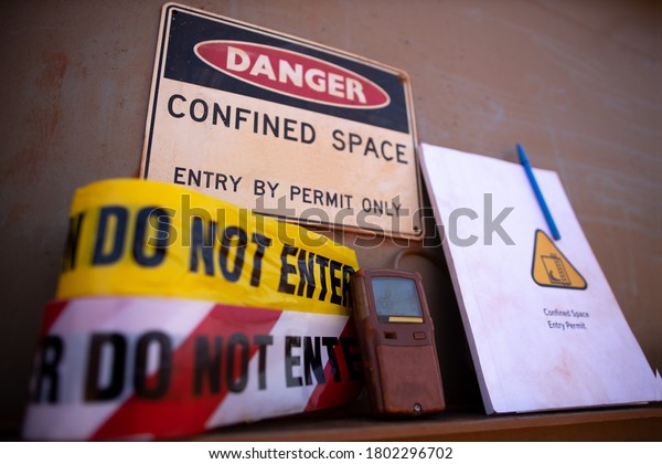 Confined space warning sign permit entry by permit only\
and red barricade danger tape, yellow caution tape gas test leak\
atmosphere with defocused confined space permit book template, pen \
background 