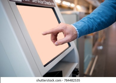 Confirm flight details. Close-up of male hands is using self-service check-in kiosk while standing at international airport building. He is registering on his airplane