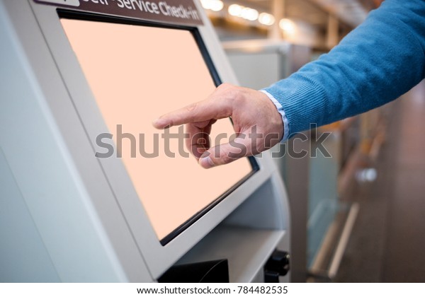 Confirm flight details.\
Close-up of male hands is using self-service check-in kiosk while\
standing at international airport building. He is registering on\
his airplane