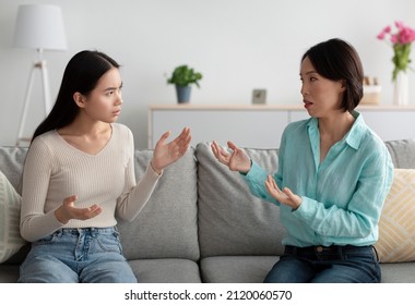 Conflict between generations, family crisis concept. Unhappy mature Asian woman and her adult daughter having fight, arguing with each other on couch in living room