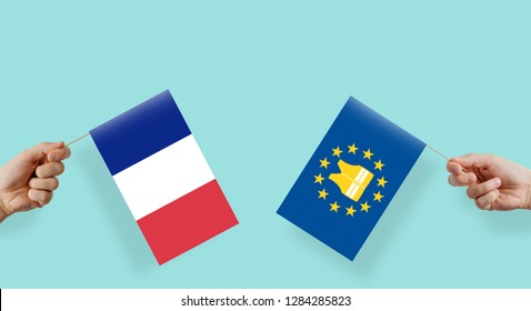 Conflict in France between the government and the yellow vests. Hands hold the france flag and the EU flagship with a yellow vest. Crisis in France, protests and problems with society.