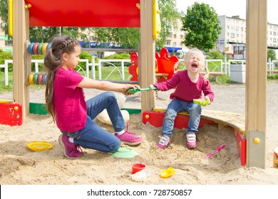 Conflict on the playground. Two sisters fighting over a toy shovel in the sandbox. Kid sister crying all throat 