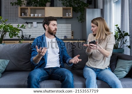 Conflict, quarrel, jealousy in the family home. Young couple, man and woman. The woman is jealous, takes the phone from her husband, demands an explanation