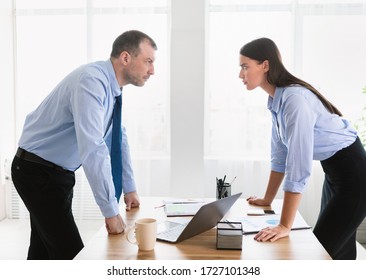 Conflict At Work. Businessman And Businesswoman Staring At Each Other Arguing Having Confrontation Standing In Modern Office.
